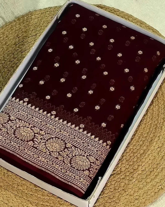 A dark maroon velvet fabric, likely a saree, displayed inside its clear plastic packaging. The fabric features small metallic gold floral motifs and a detailed gold zari border.