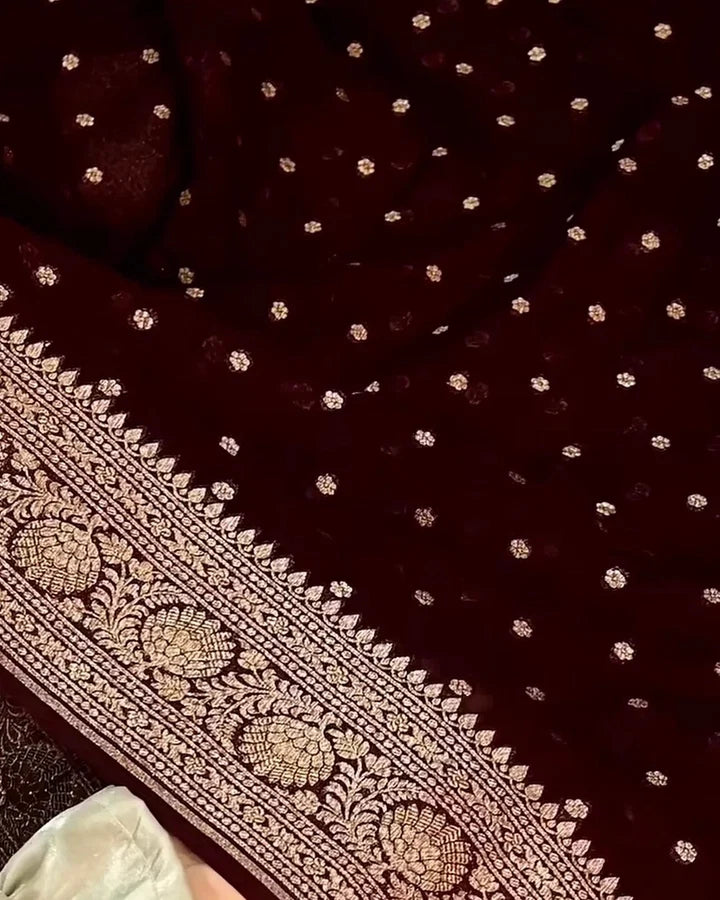 A close-up of a deep maroon velvet fabric with small metallic gold floral motifs scattered across it and a wide ornate gold brocade border along one edge.