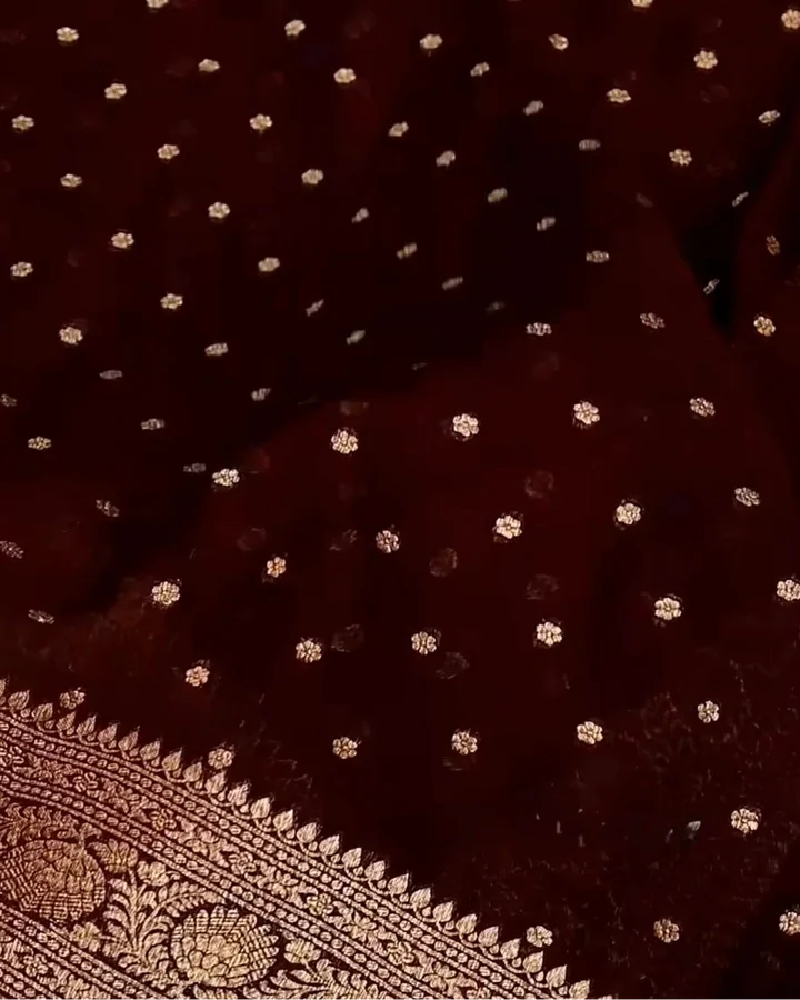 A close-up of a deep maroon fabric with scattered small gold floral motifs and a decorative gold border along the bottom edge.