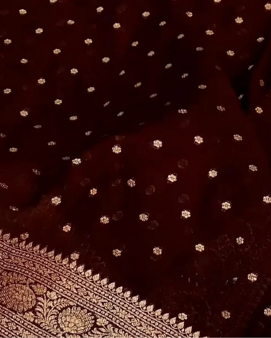 A close-up of a deep maroon fabric with scattered small gold floral motifs and a decorative gold border along the bottom edge.