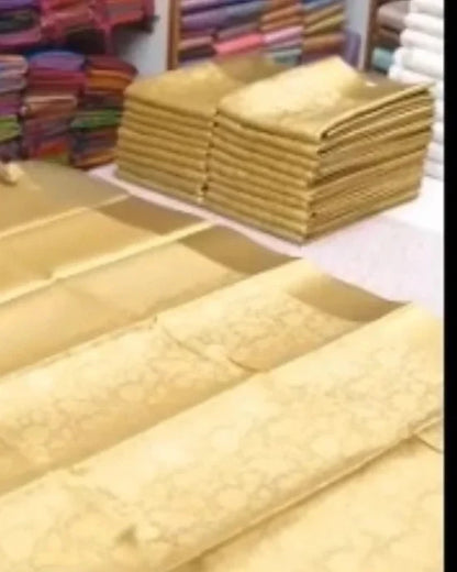 Gold patterned fabric displayed on a table, with stacks of folded matching fabric in a shop setting.