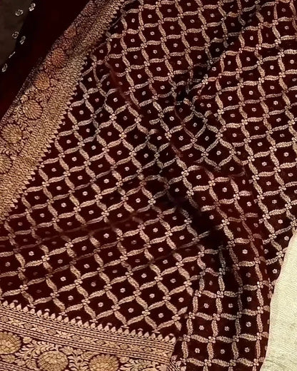 A close-up of a dark brown fabric with an intricate beige geometric lattice pattern and ornate woven borders.